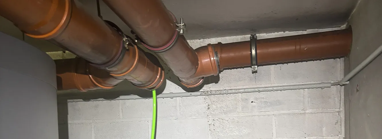 Des tuyaux de plomberie en plastique marron fixés au plafond et au mur en béton à l'aide de colliers métalliques.s.